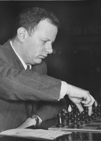 A black and white photo of Isaac Boleslavsky, about to play a pawn move for black with a set of Hungarian chessmen. 