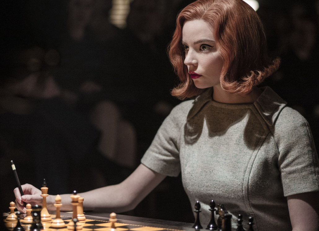 Anya Taylor-Joy as Beth Harmon writes a move on a score sheet in front of a set of Morodovian-Latvian chessmen.