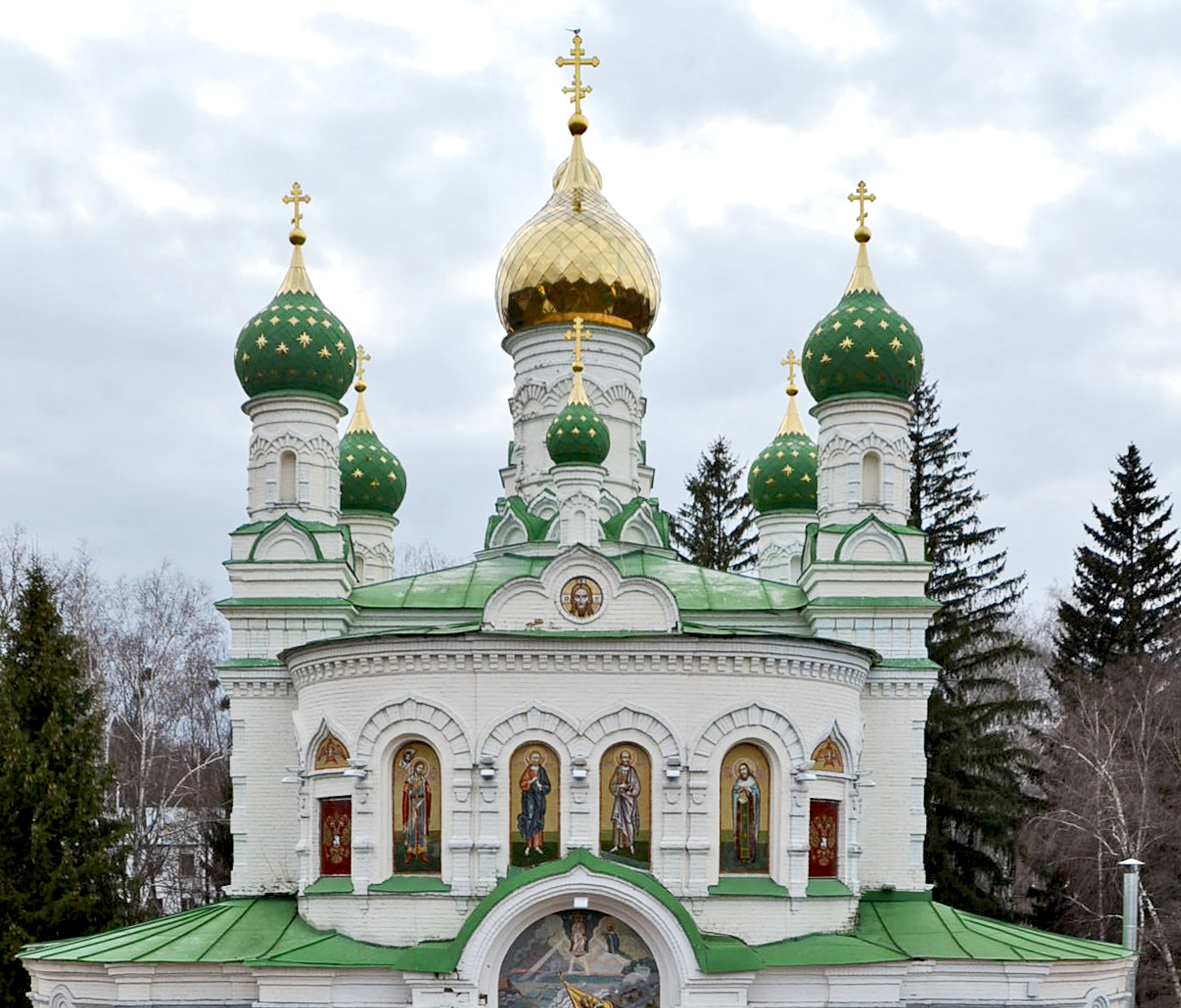 The roof of a white stone cathedral. Its roof is green, and in the centre is a tower with a golden onion dome. The tower is surrounded by smaller towers with green domes with and gold elements.